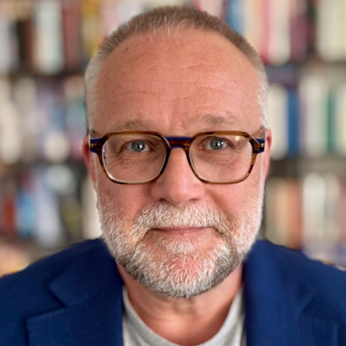 Headshot of a person with glasses, short grey hair, and a beard, wearing a blue jacket.