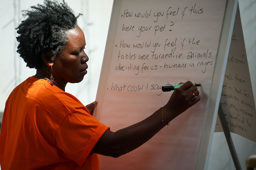 Person in an orange top writing questions about animals and humans on a flipchart.