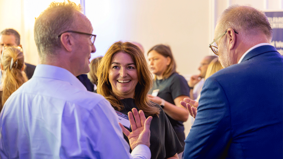 Photograph of three guests talking together, a brown haired woman is in the centre of the image.